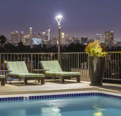 Apartments in Hancock Park with a pool and lounge chairs, offering a breathtaking view of the city at night.