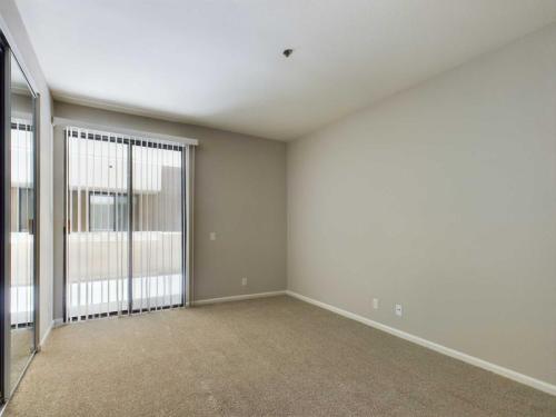 Apartments in Hancock Park, CA An empty room with beige carpet, light gray walls, sliding glass door with vertical blinds, and a mirrored closet door. Chelsea Court Apartments in Hancock Park 500 North Rossmore Avenue Hancock Park, CA 90004  P: 833-918-2899 TTY:711 F: 323-446-8466